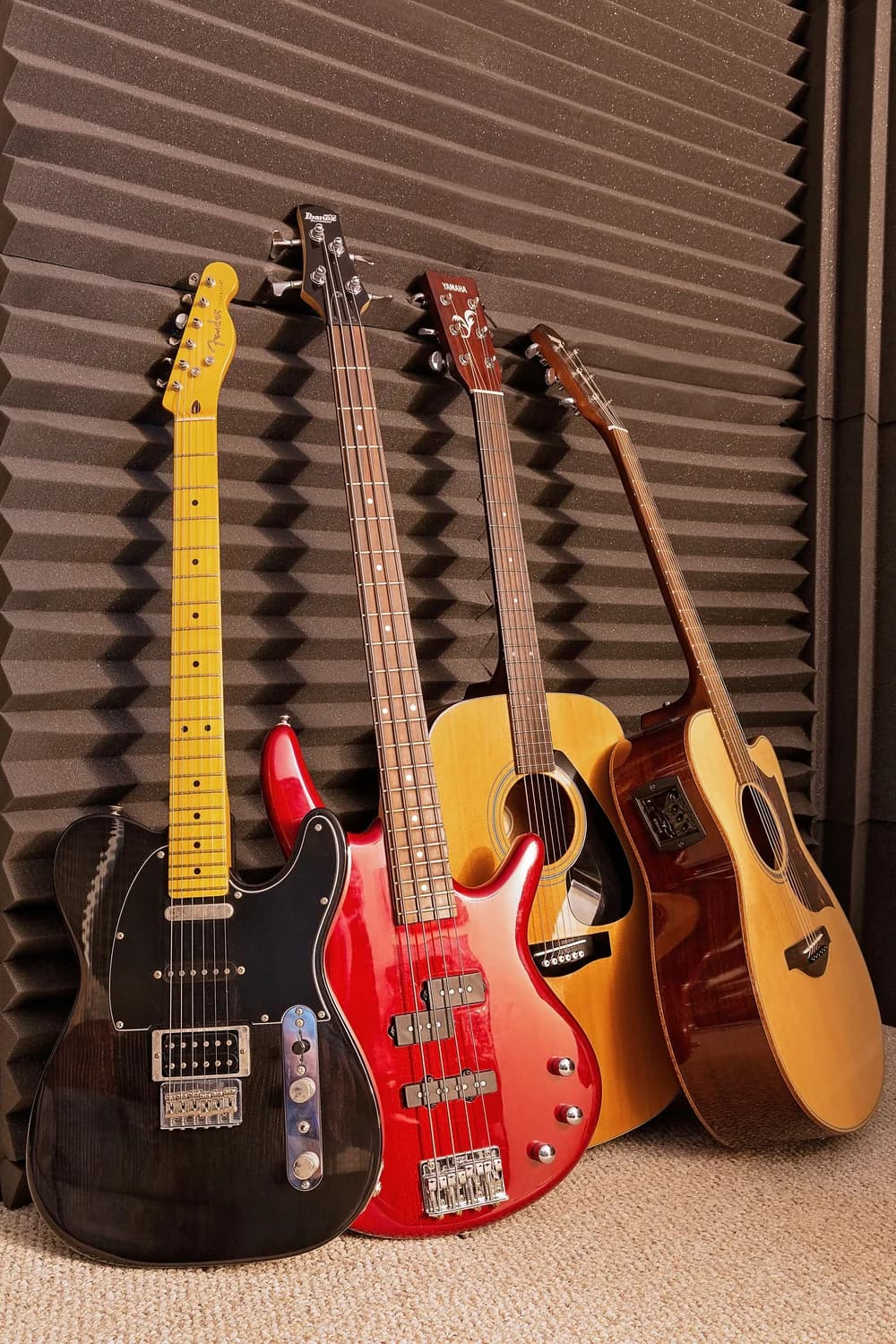 A Fender Telecaster, an Ibanez bass, and two acoustic guitars leaning against acoustic foam