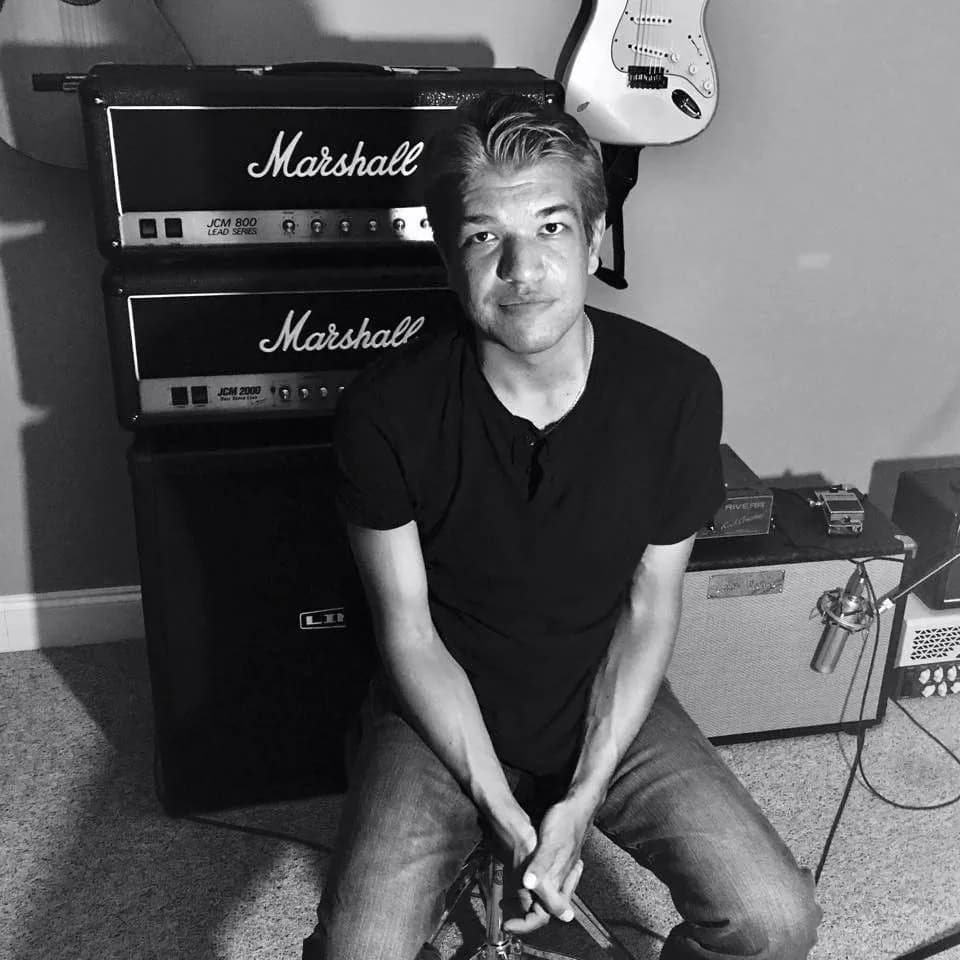 Eli Fortner seated in front of a stack of Marshall guitar amplifiers, in black and white